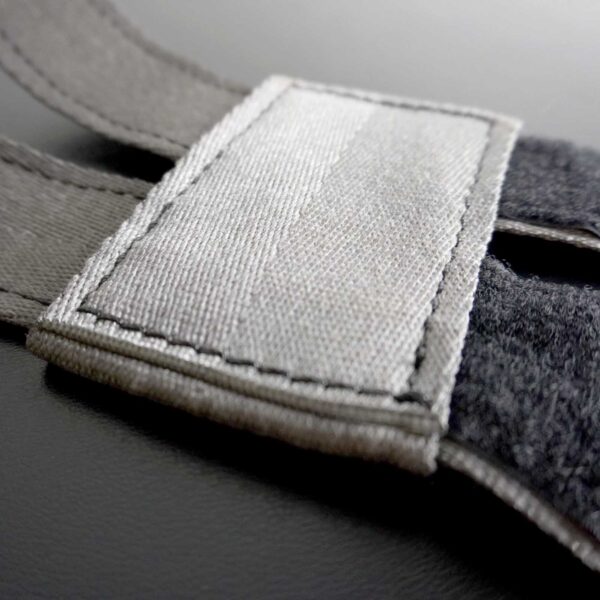 Close-up of the gray fabric strap from the Spud Inc 5R Barbell Shield, featuring a Velcro patch on a black surface. The detailed texture highlights visible stitching around the Velcro edges.