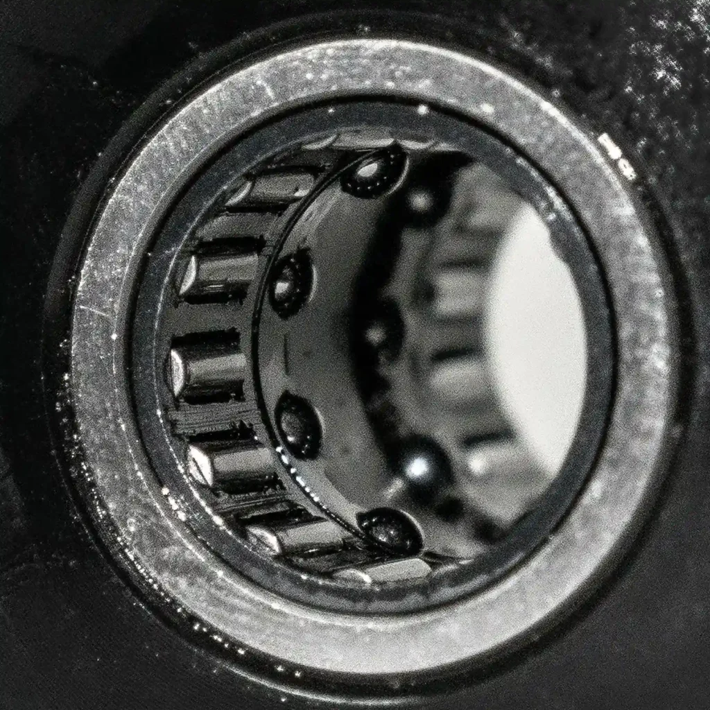 Close-up of a metal bearing with cylindrical rollers arranged around the inner ring, reminiscent of the smooth, precise motion found in an ATX Compact Leg Press. The shiny surface reflects light, and the bearing is set within a dark circular frame.