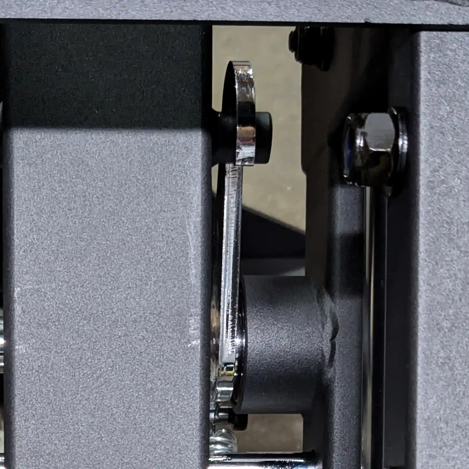 Close-up of a metal mechanism featuring bolts and levers, reminiscent of components on the ATX Compact Leg Press. The image reveals a gray, textured metal surface with a shiny lever and fastener that might be part of intricate machinery or fitness equipment like the sled leg press.