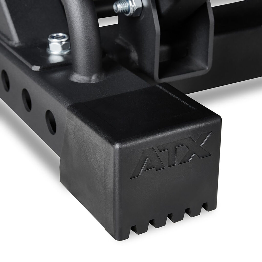 Close-up of a black metal component with a textured plastic cap showing ATX letters. Visible bolts and a perforated metal bar suggest its part of the ATX® Leg Press/Hack Squat 4in1 Combo fitness equipment.