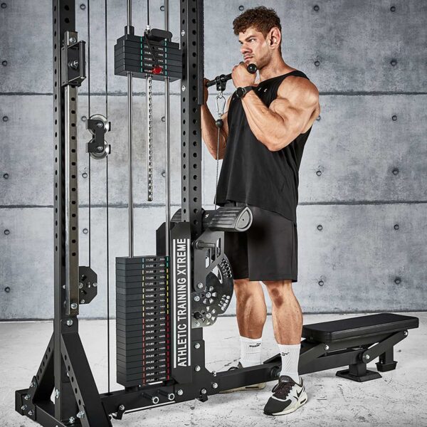 A muscular person in a black tank top and shorts performs a bicep curl on the ATX® Trinity Tower 135 kg cable machine in a gym, set against a concrete wall.
