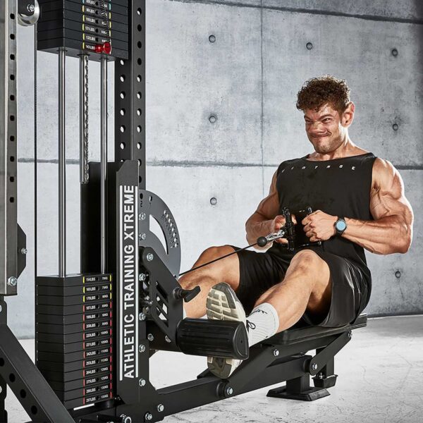 A person intensely working out on an ATX® Trinity Tower 135 kg cable row machine in a gym with a concrete wall background, wearing a black tank top, shorts, and white sneakers.