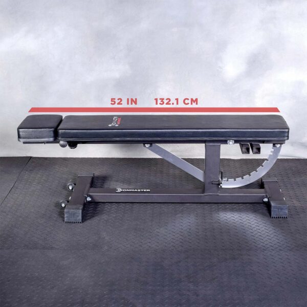 A black Ironmaster Head Extension SB adjustable gym bench sits on a black rubber floor against a gray wall, featuring a 52-inch (132.1 cm) measurement line on its frame.