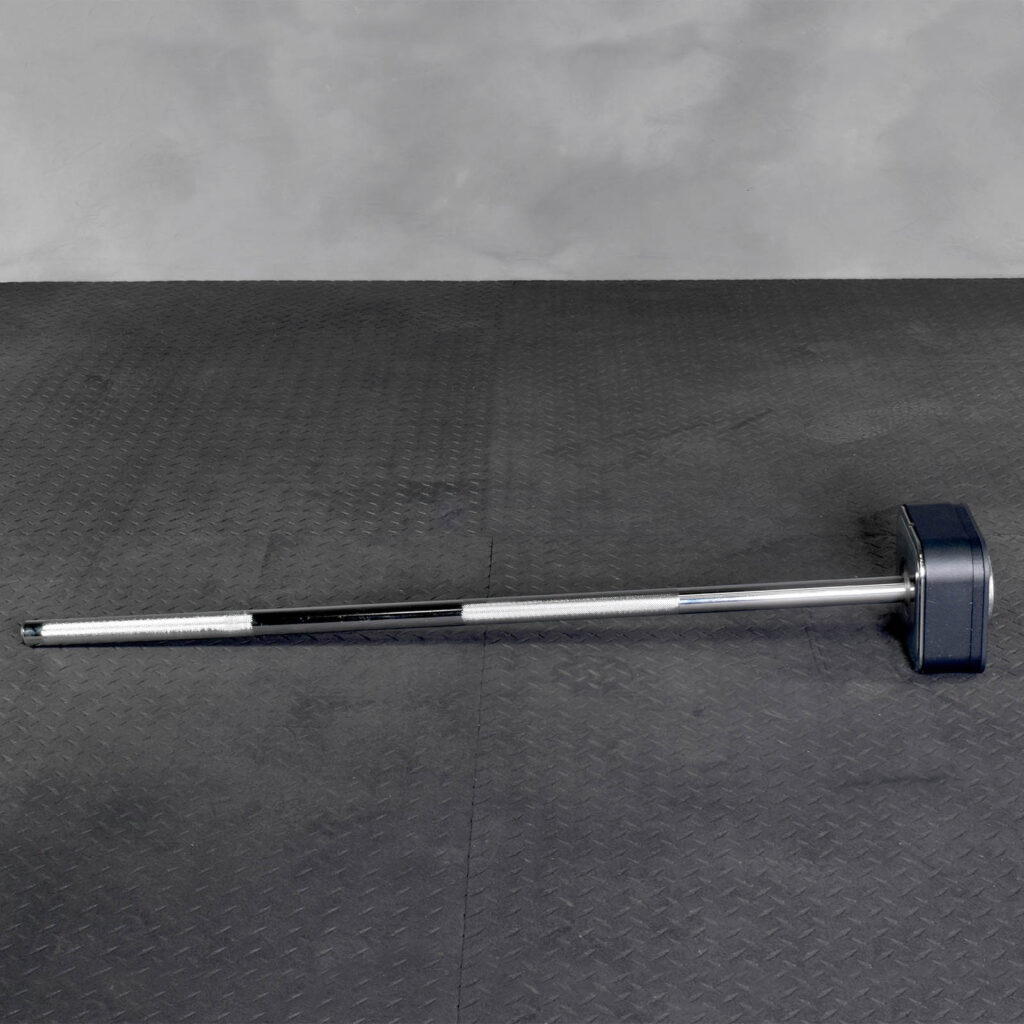 The Ironmaster Quick Lock Mace Handle, featuring a robust, long metal grip and large square rubber head, rests on a textured dark gray floor with a plain gray wall in the background.