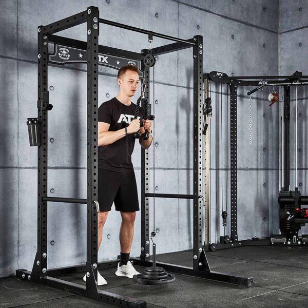 Wearing a black t-shirt and shorts, a person uses the Cable Pulley System (High) in a gym with gray concrete walls and black equipment featuring metal accents.