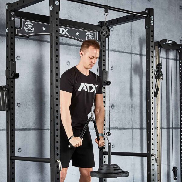 Wearing a black ATX shirt, someone performs a tricep pulldown using the Cable Pulley System (High) on an ATX power rack, set against a sleek gray concrete wall.