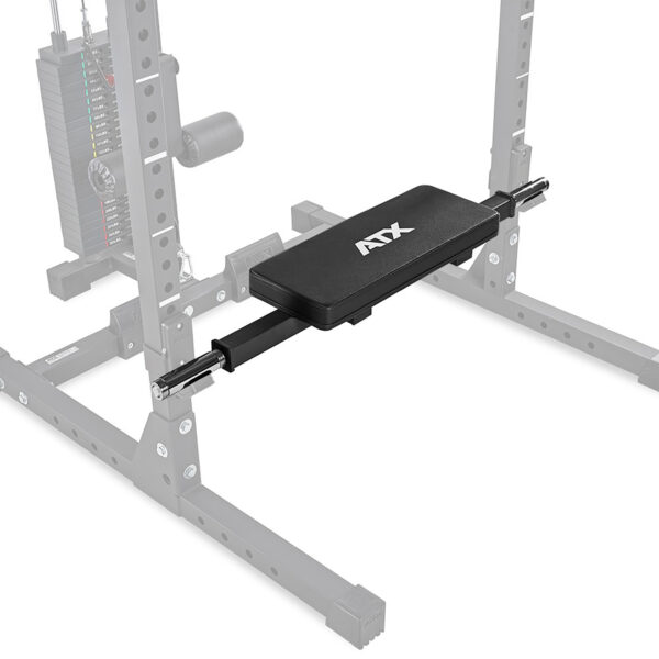 A gym setup includes a black bench pad with ATX printed on it, attached to an adjustable cable crossover machine. The ATX® Hip Thruster Attachment complements the sturdy metal frame and visible pulley system in the background.