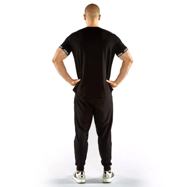 A person stands with their back to the camera, wearing an ATX® Training Shirt BLACK and pants with white sneakers. Their hands are on their hips against a plain white background.