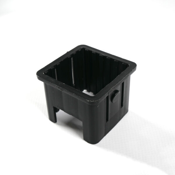An Upright Sleeve Insert 40x40, a black rectangular plastic container with open ends and a button-like feature on one side, stands on a white surface.