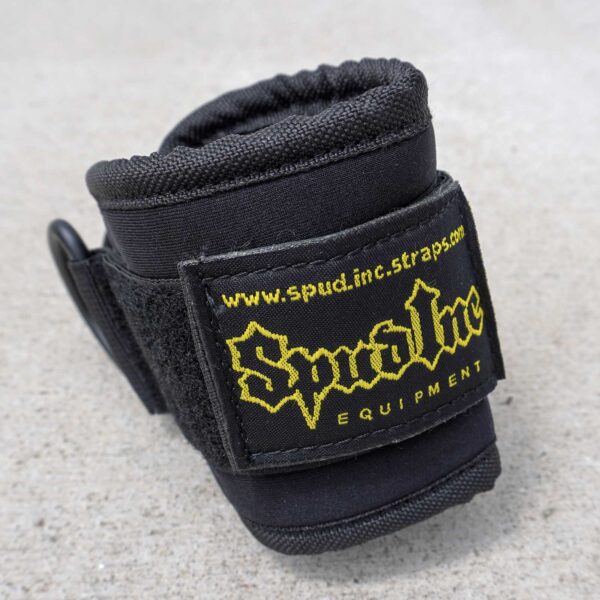 Close-up of a black Spud Ankle Cuff with a Velcro strap featuring the yellow Spud Inc Equipment label and the website www.spud.inc.straps.com, all on a gray surface.