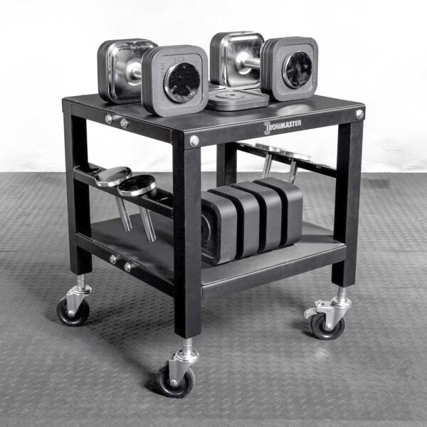 The Ironmaster QLDB Stand PRO showcases a modern black design with square-shaped adjustable dumbbells on wheels. It features two shelves for extra weights and accessories, all sitting on a durable rubber mat.