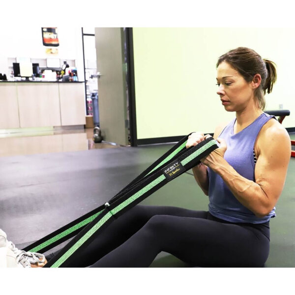 A woman in athletic wear sits on a gym floor, using the Spud Inc Infinity Loop for an arm workout. She appears focused, surrounded by visible gym equipment in the background.
