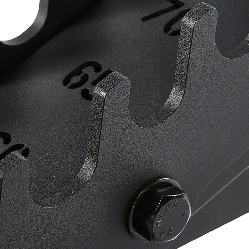 Close-up of a black, textured metal surface on the ATX® Warrior Bench 2.0, featuring a bolt and evenly spaced numbered notches (6-9) in a curved design, resembling a gear or mechanical component.