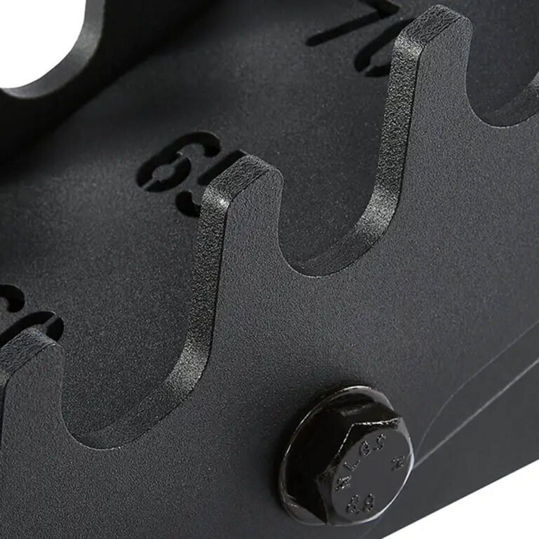 Close-up of a black, textured metal surface on the ATX® Warrior Bench 2.0, featuring a bolt and evenly spaced numbered notches (6-9) in a curved design, resembling a gear or mechanical component.