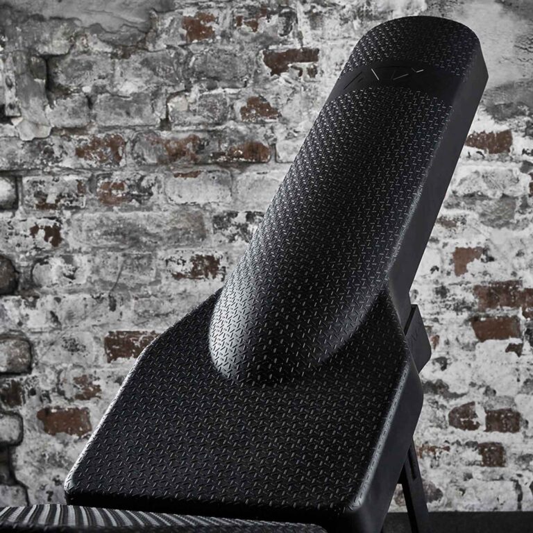 Close-up of an adjustable gym bench against a rustic brick wall. The weight bench features a black diamond-patterned surface, suggesting durability and comfort for fitness use.