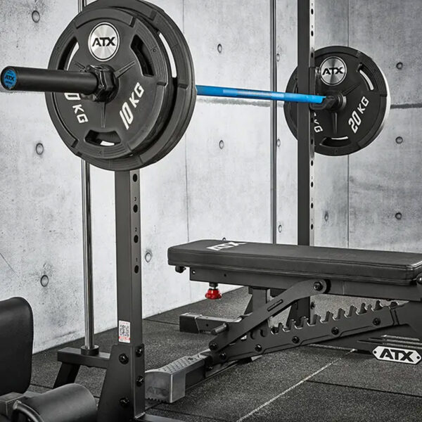 An ATX® Smith Machine 500 setup featuring a black adjustable bench, barbell with 20 kg and 10 kg plates on each side, set against a gray concrete wall and padded flooring, ideal for areas with low ceilings at just 198 cm high.