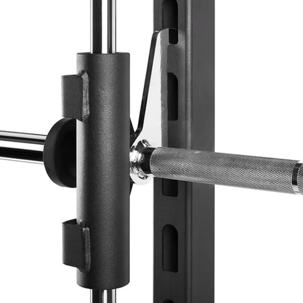 A close-up of the ATX® Smith Machine 500 shows a weightlifters barbell with a knurled grip on a rack with safety hooks. The 198 cm tall machine features adjustable slots and is ideal for gym or fitness center setups, especially in low-ceiling environments.