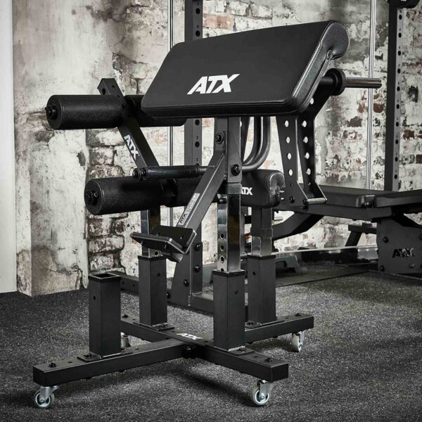 An ATX® Attachment Storage Rack is set against exposed brick walls in a room. It features padded supports, an adjustable frame, and multiple padded bars for leg workouts. The floor is carpeted in dark gray.