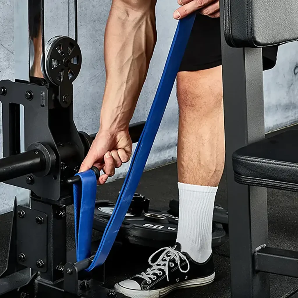 A person in shorts, socks, and black sneakers adjusts a blue resistance band on an ATX® Pec Fly/Rear Delt Machine. A weight plate is visible on the floor nearby.