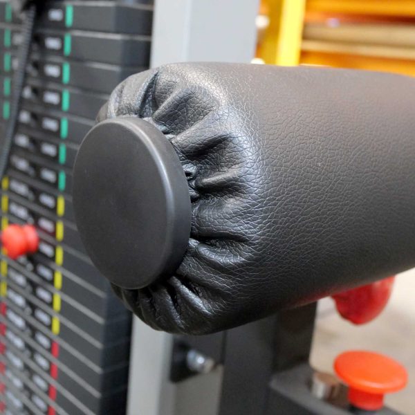 Close-up of a gym machines padded, cylindrical armrest, featuring a black Foam Roller Cover 65mm. A stack of adjustable weights is visible in the background, with numbered markings and colored lines next to red adjustment knobs.