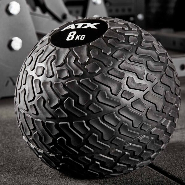 Close-up of an ATX® Slam Ball 8 kg featuring a textured surface for grip, resting on a gym mat with blurred fitness equipment in the background.