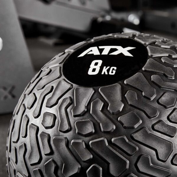 Close-up of a black ATX® Slam Ball labeled 8 KG with a textured surface, set against a blurred gym background.