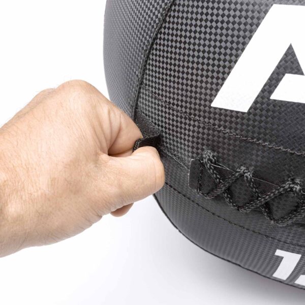 A hand gripping the strap of an ATX® Wall Ball PVC, featuring a textured black surface with visible stitching and a partial white printed letter.