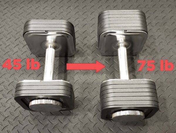 Two Ironmaster adjustable dumbbells rest on a black textured floor, with the left labeled 45 lb and the right labeled 75 lb. A red arrow points from the left dumbbell to the right, suggesting progression in your workout.