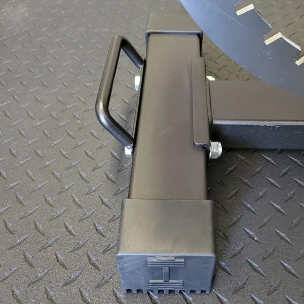 Close-up of the Ironmaster Bench Handle on a textured rubber floor. This sturdy, rectangular black base with bolt connections supports a larger round component above, highlighting its robust construction crucial for an intense exercise workout bench setup.