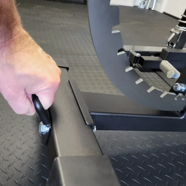 On a rubberized floor, a persons hand grips the Ironmaster Bench Handle, which features a notched, circular metal piece for adjusting angles or positions during workouts.