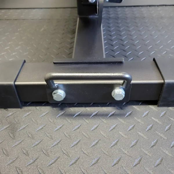 Close-up of an Ironmaster Bench Handle, secured with bolts to a black bar on a textured floor. The diamond plate pattern suggests it is part of sturdy exercise equipment like the Ironmaster Super Bench PRO.