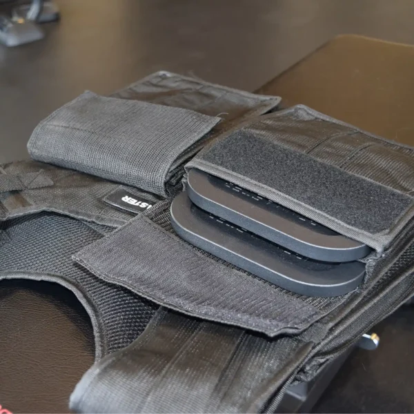 Close-up of the Ironmaster Ultimate Training Vest, a black tactical vest with visible removable ballistic plates in the front compartments. This versatile vest, designed like a fitness vest, is displayed on a dark surface, highlighting its storage pockets and protective features.