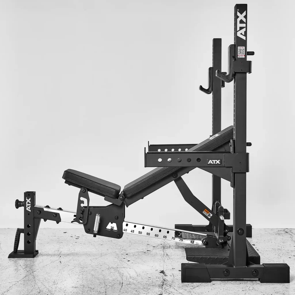 The ATX® Adjustable Bench Press is a black adjustable commercial bench with a built-in squat rack, slanted backrest, and barbell holders. It is shown on a gray concrete floor against a white wall.