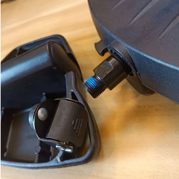 Close-up of a black Spin Bike Pedal MATRIX 9/16 featuring a blue threaded nozzle attached to a black device, set against a light wooden background.