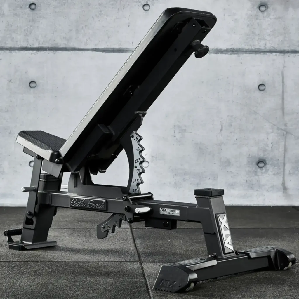 The ATX® Warrior Bench - Slim PU (Copy) sits on a dark gym floor against a concrete wall backdrop, featuring a padded seat and backrest with clearly visible numerical adjustments for incline settings.