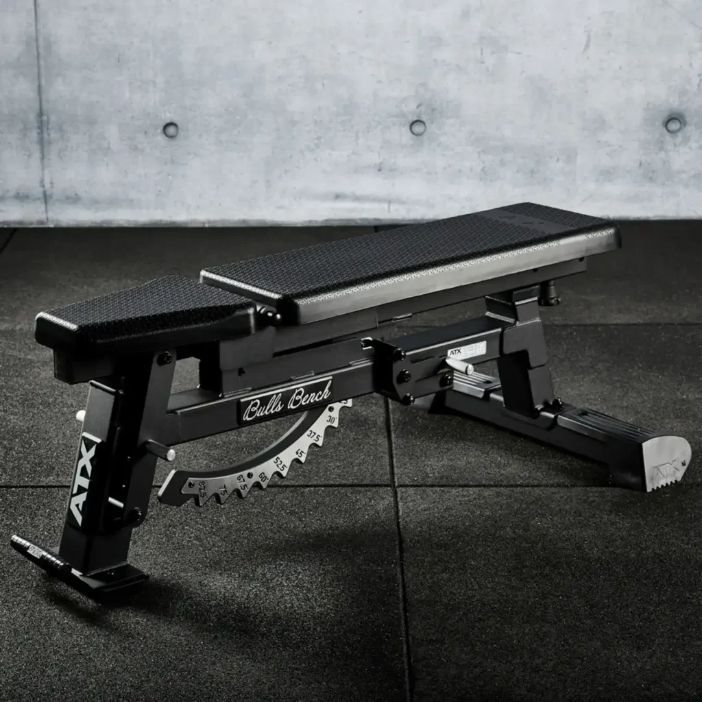 An ATX® Warrior Bench - Slim PU is positioned on a dark rubber gym floor, showcasing multiple incline options and a durable metal frame. The brand ATX is visible on the side, set against concrete walls in the background.
