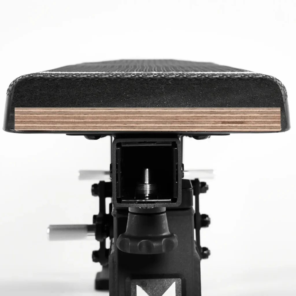 Close-up of the ATX® Warrior Bench - Slim PUs black seat with layered wooden detailing underneath, attached to a metal support in a stationary setup against a white background.