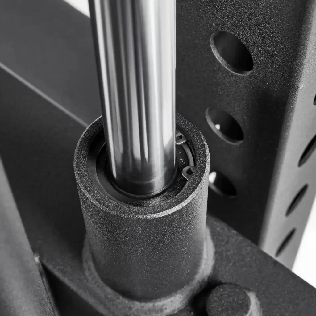 Close-up of a shiny metallic rod inserted into a sturdy, dark-colored holder with a textured surface. The rod is part of a mechanical structure, with holes visible in the nearby metal, suggesting an industrial or equipment setting.