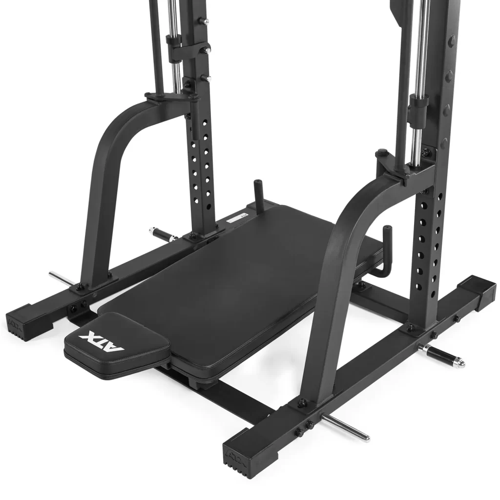 Close-up of a black weightlifting bench and squat rack. The bench is flat and has the brand ATX on the edge. The rack features adjustable safety bars and support rails, with a sturdy metal frame designed for heavy lifting exercises.