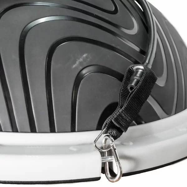 Close-up of a black and white Power Maxx Bosu Ball featuring a textured surface, with a resistance band attached through a fabric strap via metal clip, ready for exercise use.